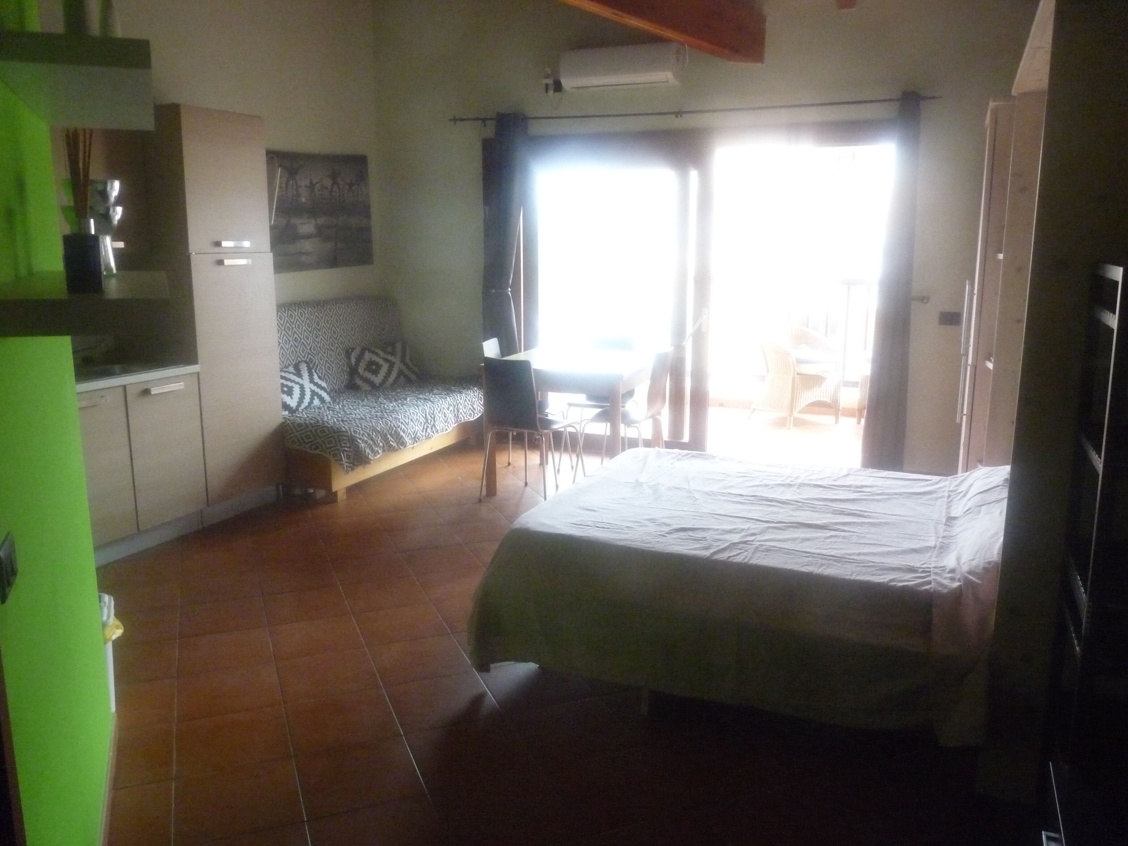 A compact room with a bed, a sofa, a dining table, and a kitchenette.