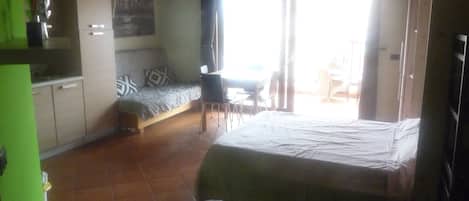 A compact room with a bed, a sofa, a dining table, and a kitchenette.