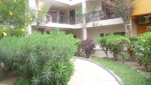Un immeuble à plusieurs étages, doté de balcons, entouré de verdure et bordé d’un sentier.
