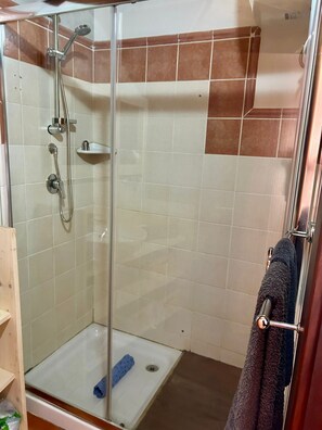 A glass-enclosed shower stall with a white floor, a blue bath mat, and a towel rack with a dark towel. - Studio apartment in beachfront complex & 2 minutes walk to town (Santa Maria)