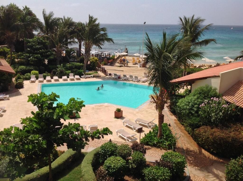 A pool area with lounge chairs and a view of the ocean.