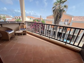 A balcony with a tiled floor, wicker furniture, and a view of neighboring buildings. - Studio apartment in beachfront complex & 2 minutes walk to town (Santa Maria)