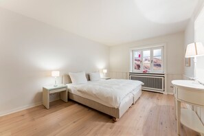 A bedroom with a bed, bedside tables, a window, and a radiator. - Heidje-Hüs - "Heidje-Hüs" Hideaway (Kampen (Sylt))