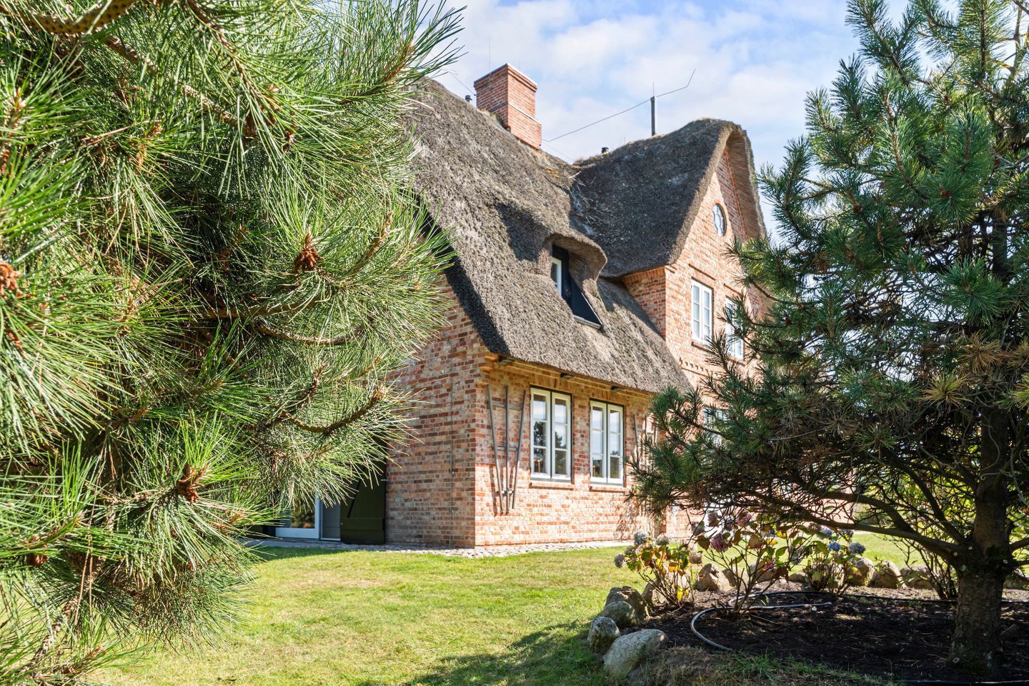 Une maison avec un toit à forte pente, des murs en briques et une pelouse bien entretenue.