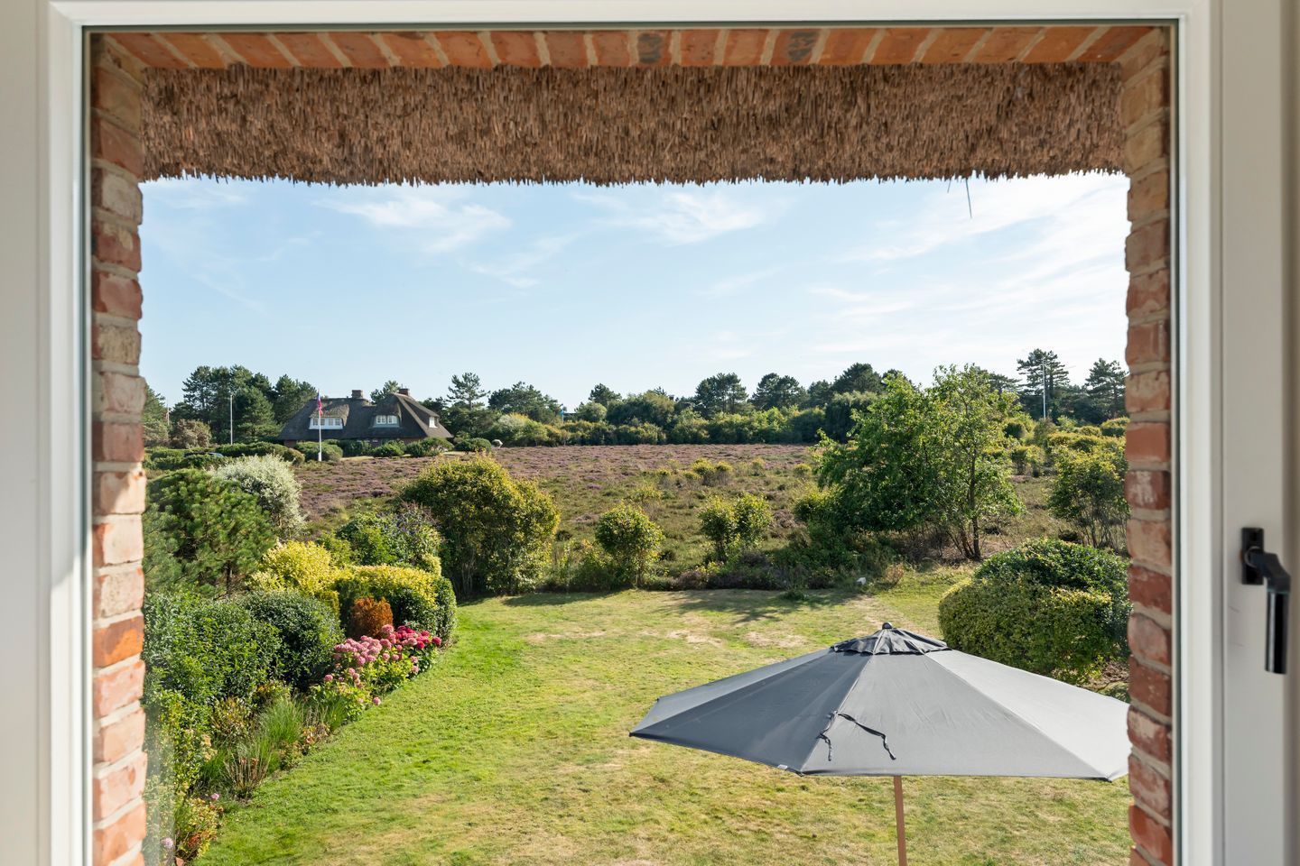 Une vue depuis l’entrée d’une maison, donnant sur un jardin avec une pelouse, une tente et une maison en arrière-plan.