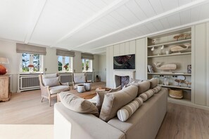 A spacious living room with a large beige sofa, a fireplace, and a bookshelf with decorative items. - Heidje-Hüs - "Heidje-Hüs" Hideaway (Kampen (Sylt))