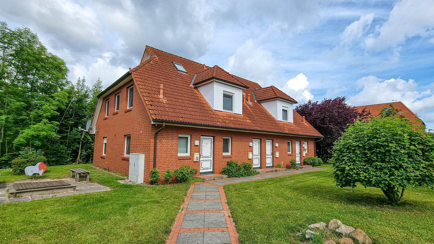 A two-story brick house with a red-tiled roof, a front porch, and a small garden.