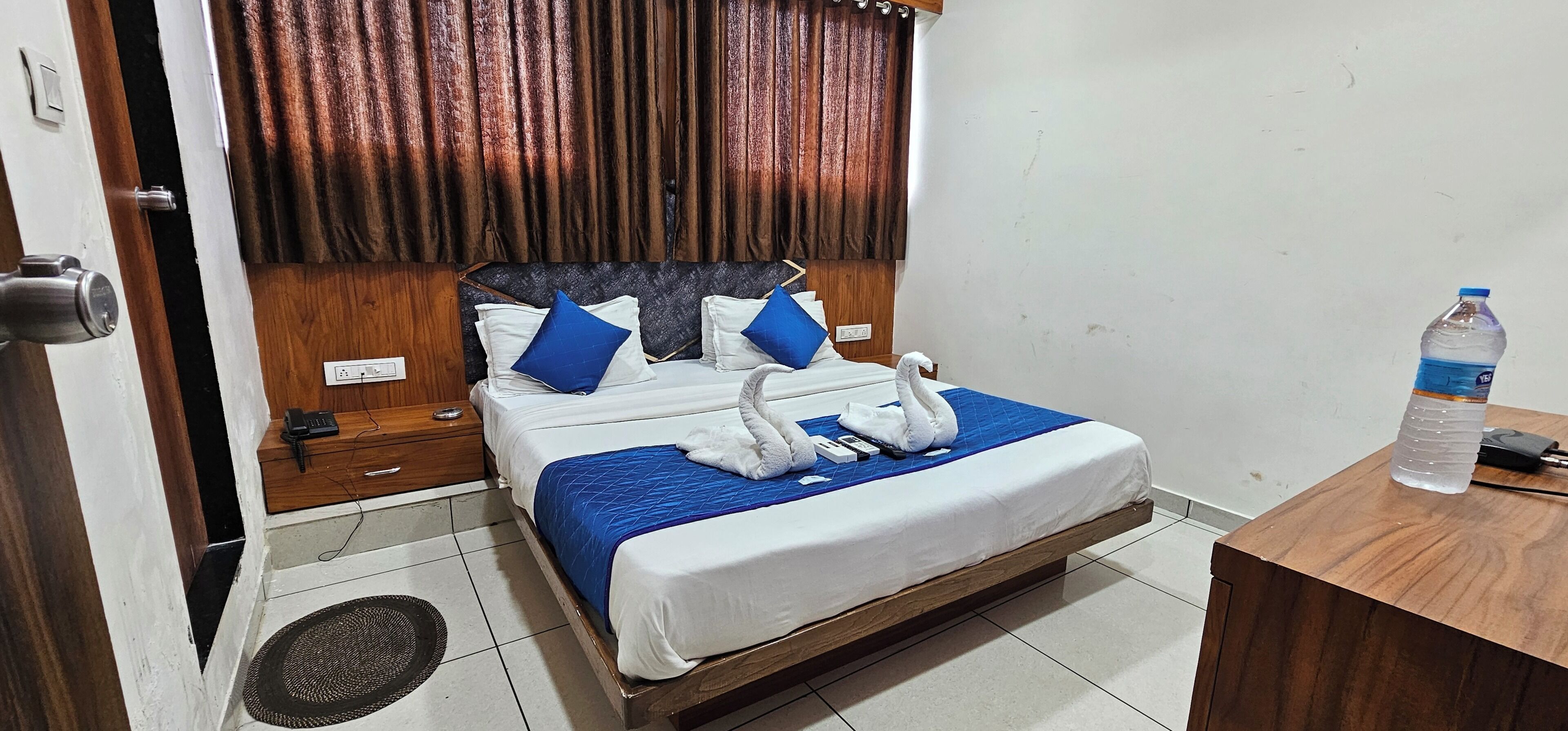 Een hotelkamer met een bed, nachtkastje, stopcontact, waterfles en afstandsbediening.