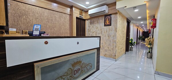 A hotel reception area with a reception desk, a framed picture on the wall, and a fire extinguisher mounted on the wall.