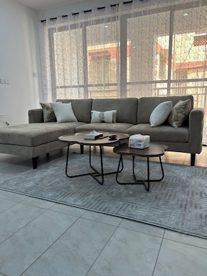A living room with a sectional sofa, two coffee tables, and a patterned rug. - 
Cozy 1 bedroom with AC and hot shower. 3 mins to the beach. Pool, gym/game room (Mombasa)