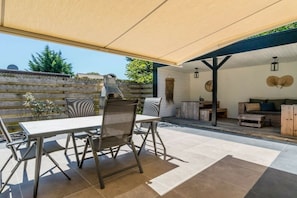 Un espacio patio al aire libre con mesa y sillas, una parrilla y una zona de estar cubierta.