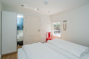 Un dormitorio con una cama, una silla roja, una ventana y una puerta.