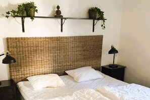 A bed with white linens, two pillows, a woven headboard, bedside lamps, and a shelf with plants. - 4 star holiday home in UDDEVALLA (UDDEVALLA)