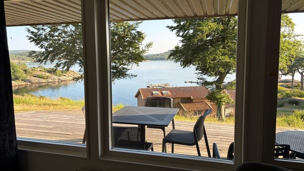 En vy över en fastighet vid sjön, med en terrass, utomhusmöbler och en byggnad med ett rött tak.