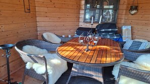 A wooden cabin interior with a round table, wicker chairs, and a fireplace. - 4 star holiday home in Sæby (Sæby)