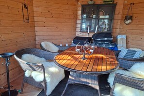 A wooden cabin interior with a round table, wicker chairs, and a fireplace. - 4 star holiday home in Sæby (Sæby)