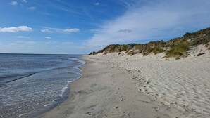 A sandy beach with gentle waves, a clear sky, and dunes in the background. - 4 star holiday home in Sæby (Sæby)