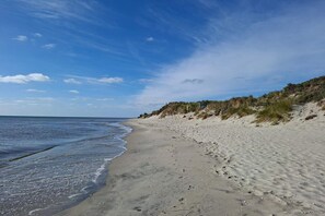 A sandy beach with gentle waves, a clear sky, and dunes in the background. - 4 star holiday home in Sæby (Sæby)