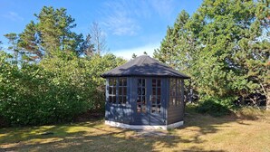 A gazebo with a peaked roof and multiple windows, surrounded by dense greenery. - 4 star holiday home in Sæby (Sæby)