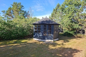 A gazebo with a peaked roof and multiple windows, surrounded by dense greenery. - 4 star holiday home in Sæby (Sæby)