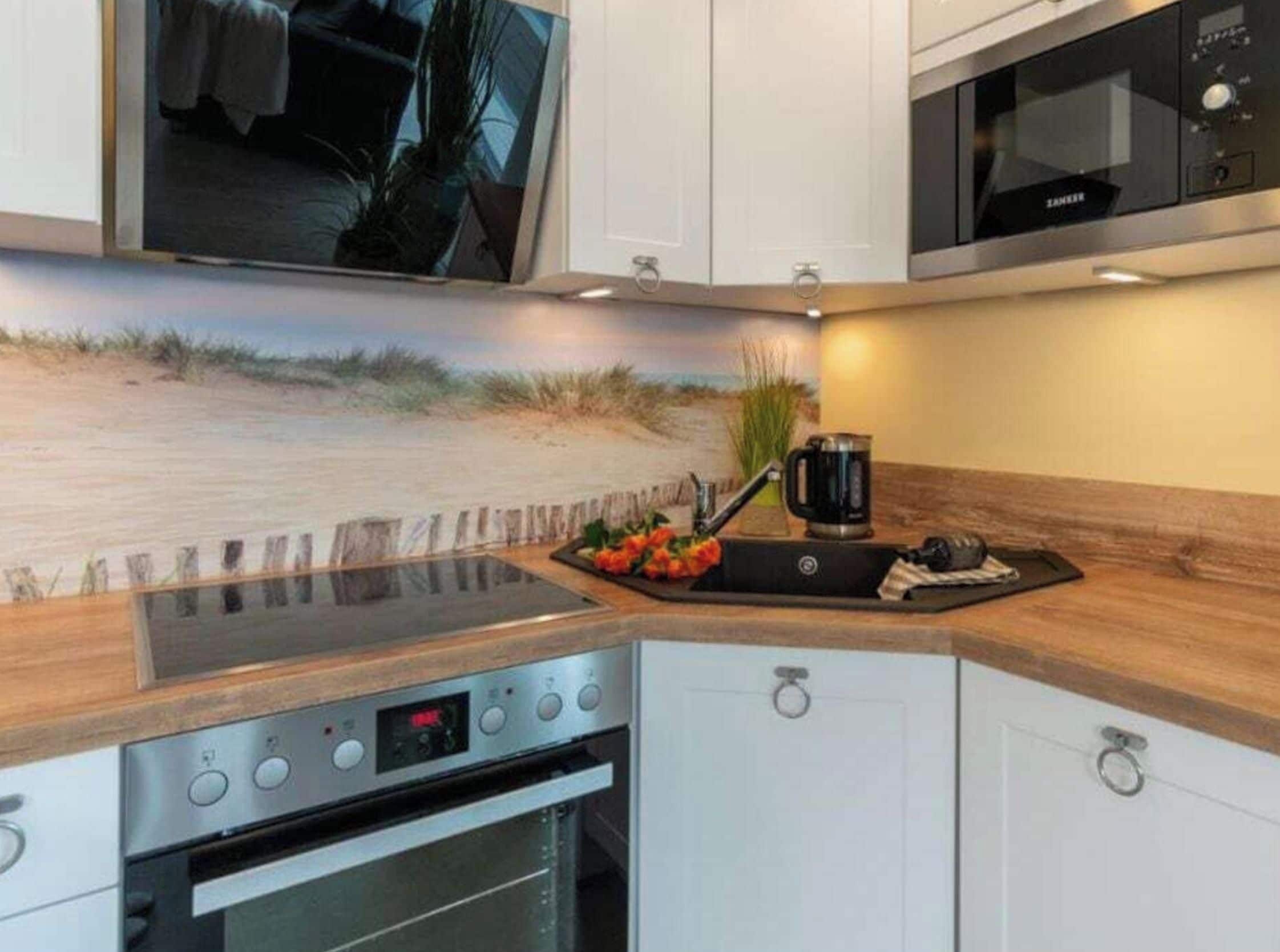 A modern kitchen with a built-in oven, microwave, and a large flat-screen TV mounted above the counter.