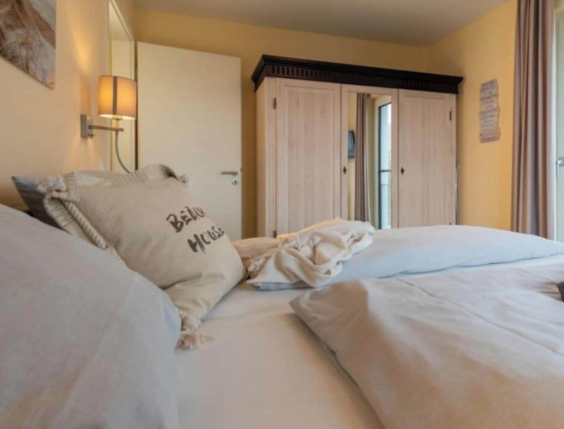 A hotel room with two beds, a large mirror, a wall-mounted lamp, and a wardrobe.