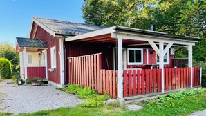 En röd trästuga med en veranda och en inhägnad trädgård.