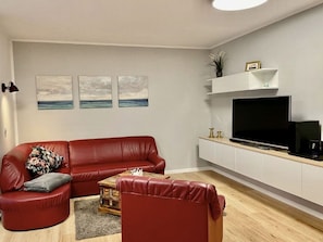 Ein Wohnzimmer mit einem roten Ledersofa, einem kleinen Holztisch und einem Flachbildfernseher auf einer weißen Unterhaltungseleinheit.