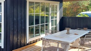 Una terrazza con un tavolo bianco e sedie in vimini, un'ampia finestra e un muro esterno scuro.