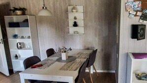 Zona pranzo con tavolo, sedie, lampadario, mobiletto bianco con ripiani e bacheca con immagini.