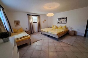 Ein Schlafzimmer mit zwei Betten, einem großen Fenster mit Vorhängen, einer Hängeleuchte und einem gerahmten Bild an der Wand.