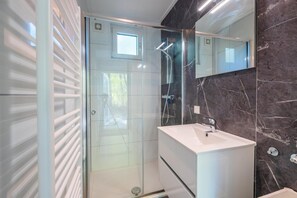 A modern bathroom with a glass shower enclosure, a white sink, and a marble-tiled wall. - Heideborg Cottage With Terrace (Ruinen)