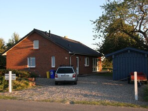 Ein zweigeschossiges Backsteinhaus mit einem Auto auf der Einfahrt, einem kleinen Schuppen und einem Kiesweg, der zum Eingang führt.