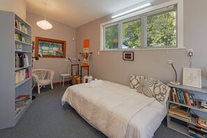 Ein Schlafzimmer mit einem Bett, einem Bücherregal, einem Sessel, einem Fenster und einem Schreibtisch.