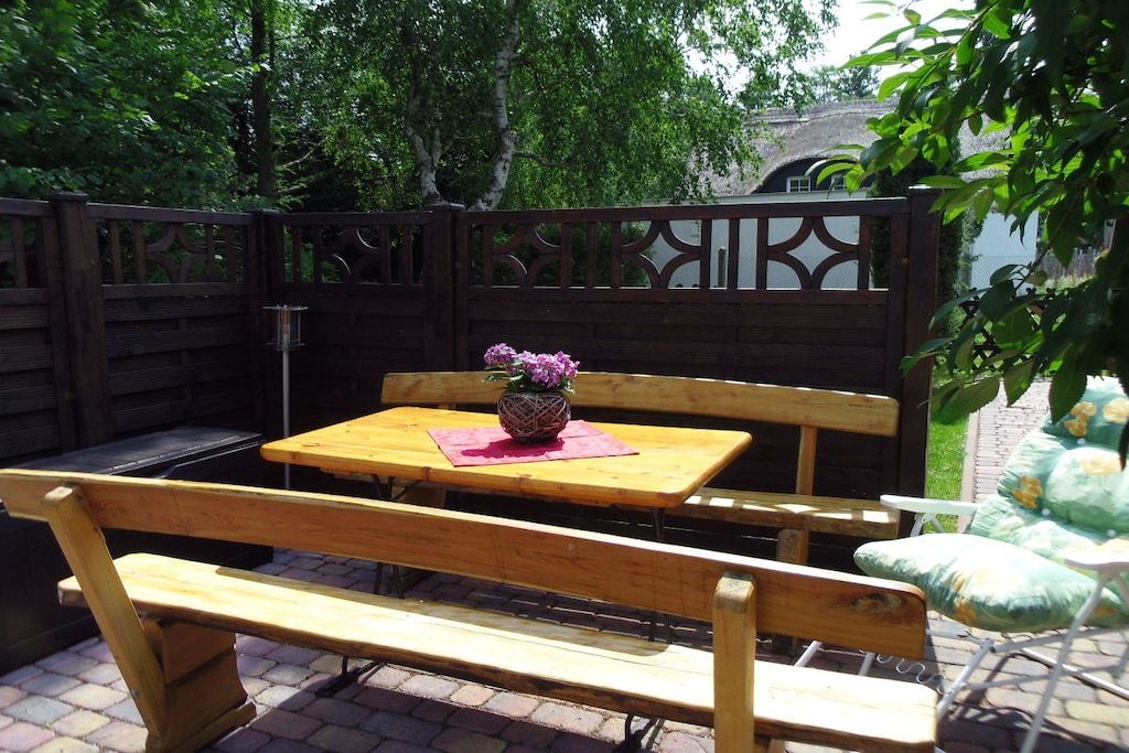 A wooden outdoor seating area with a table and benches, surrounded by a wooden fence with decorative cutouts.