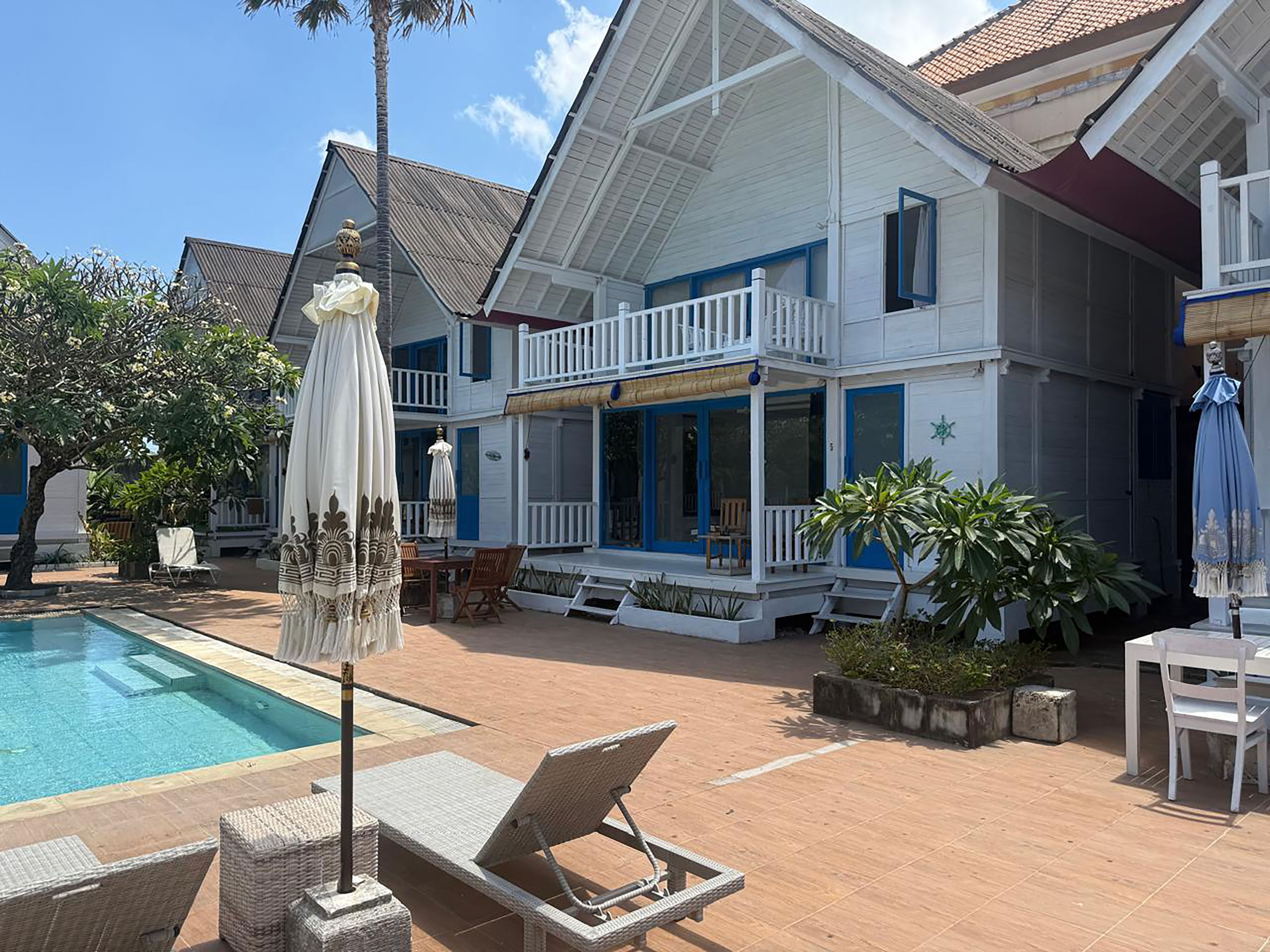 Ein zweistöckiges Haus mit Swimmingpool, Sitzgelegenheiten im Freien und einem Balkon.