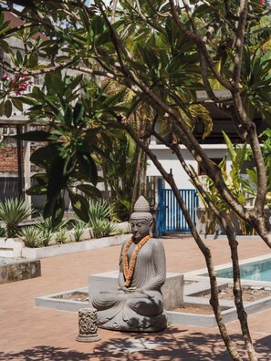 Una estatua sentada en un jardín con una piscina y un edificio al fondo.