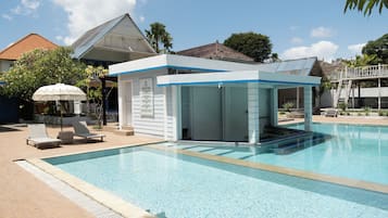 Una piscina con una zona coperta, poltrone da relax e una palma.