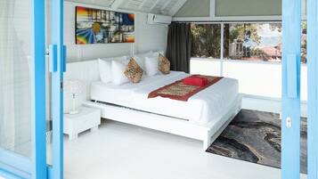 Un dormitorio moderno con cama blanca, almohadas estampadas, una manta roja y un ventanal con vistas.