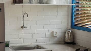 Una cocina con paredes de ladrillo blanco, un lavamanos, armarios y una ventana con persianas.