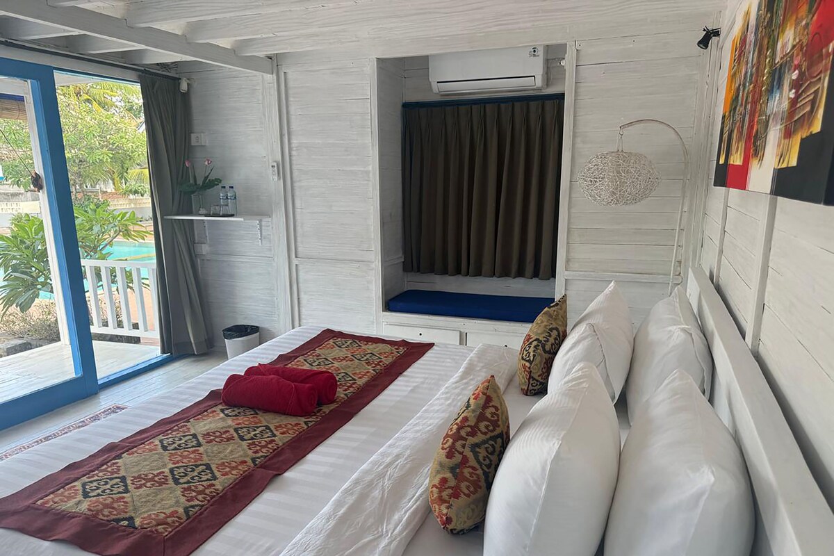 A bedroom with a bed, a window with curtains, an air conditioning unit, and a view of the outdoors.