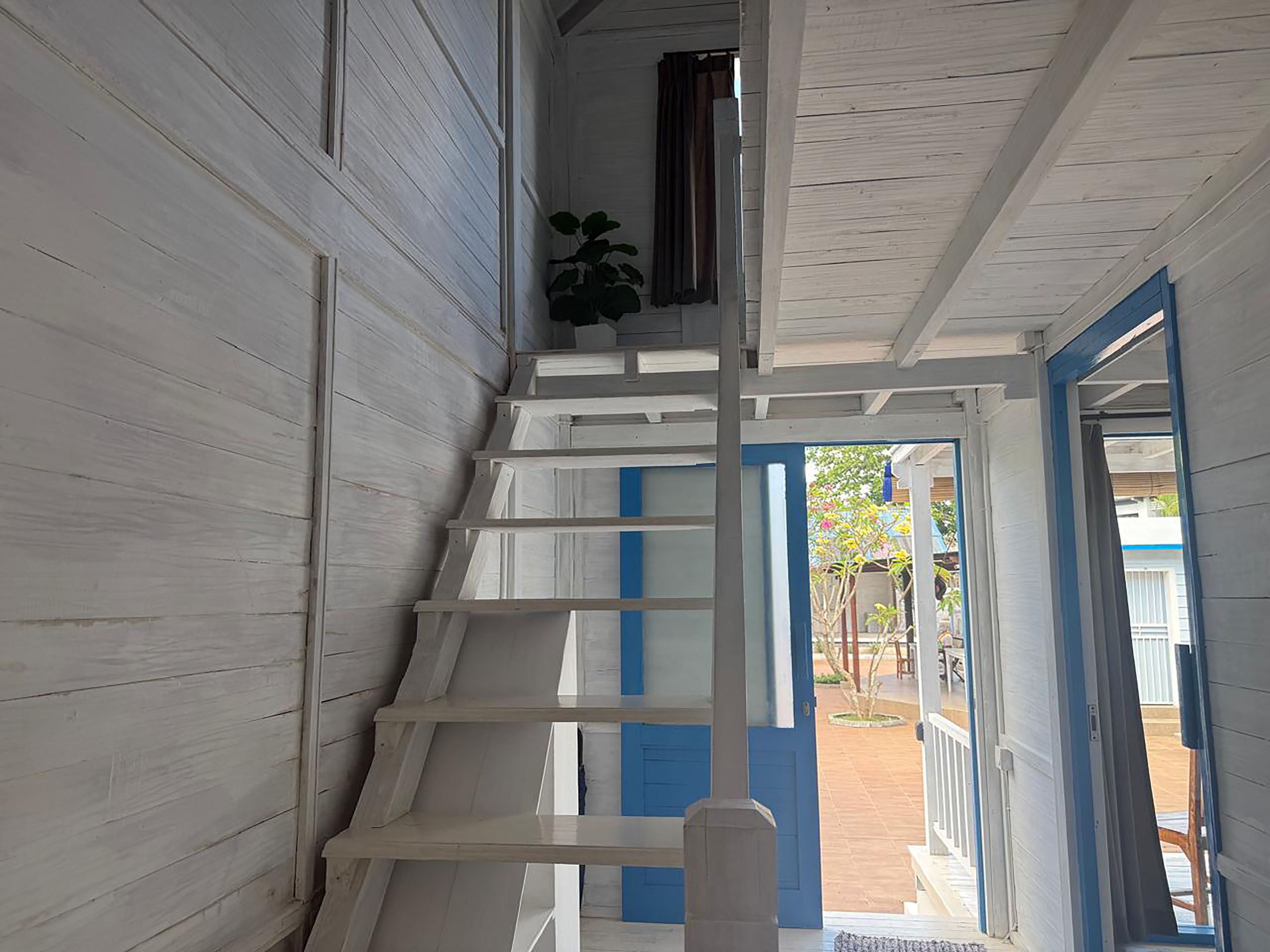 Eine Treppe mit weißen Geländern führt zu einem Außenbereich mit einer blauen Tür.
