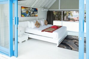 Ein modernes Schlafzimmer mit einem weißen Bett, gemusterten Kissen, einer roten Decke und einem großen Fenster mit Blick.