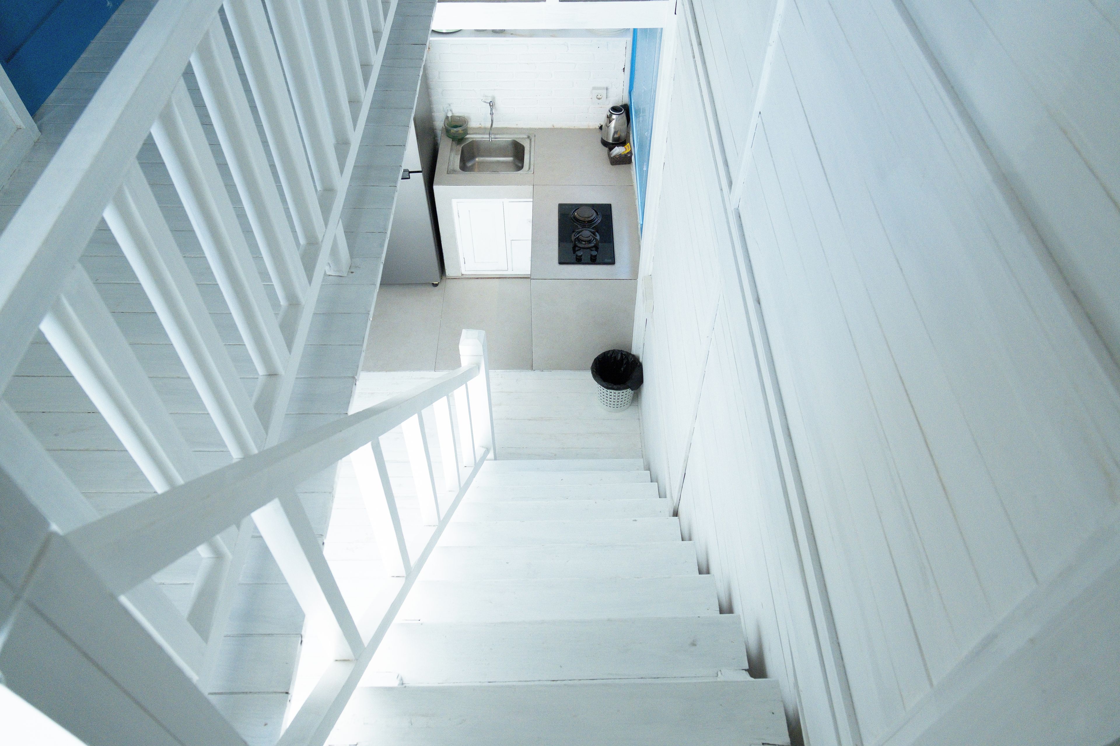 Una escalera que lleva a una zona de cocina con un lavamanos, una estufa y un cubo de basura.