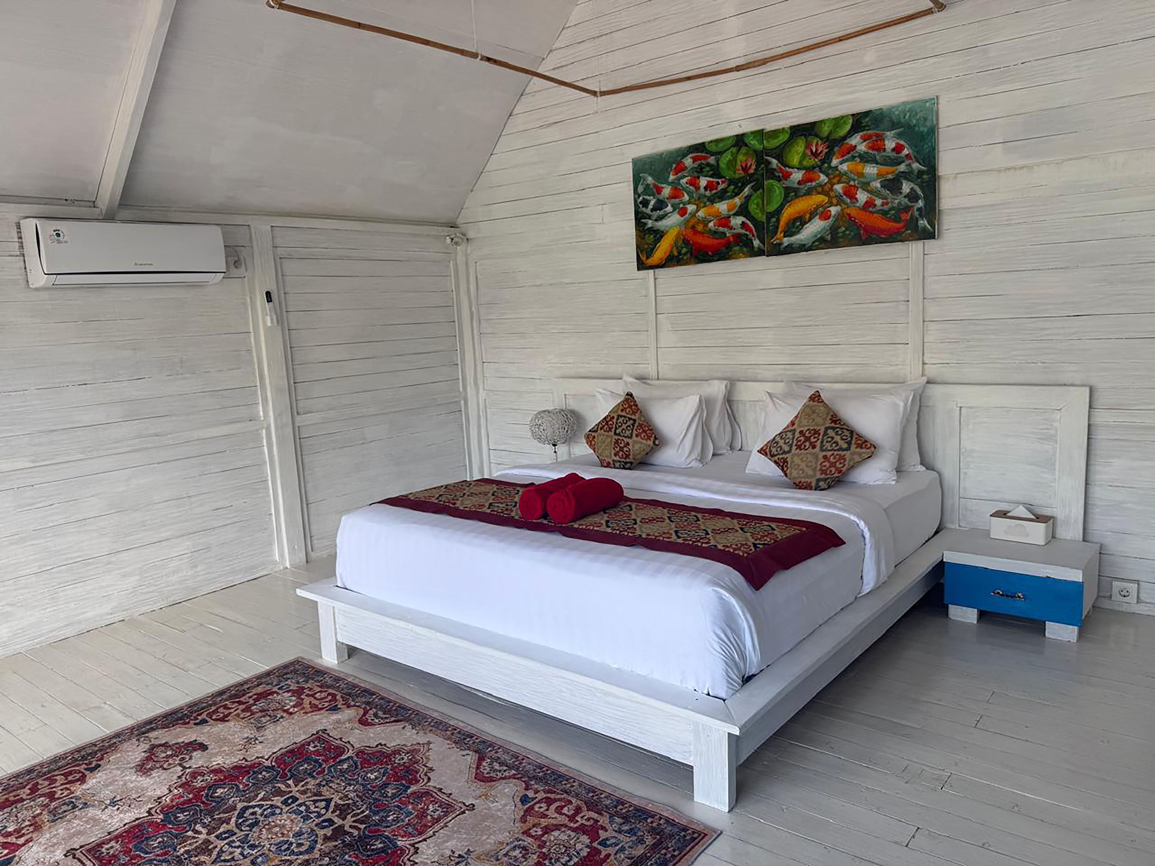 Une chambre à coucher avec un lit, des oreillers, une table de chevet, un tableau et un tapis.