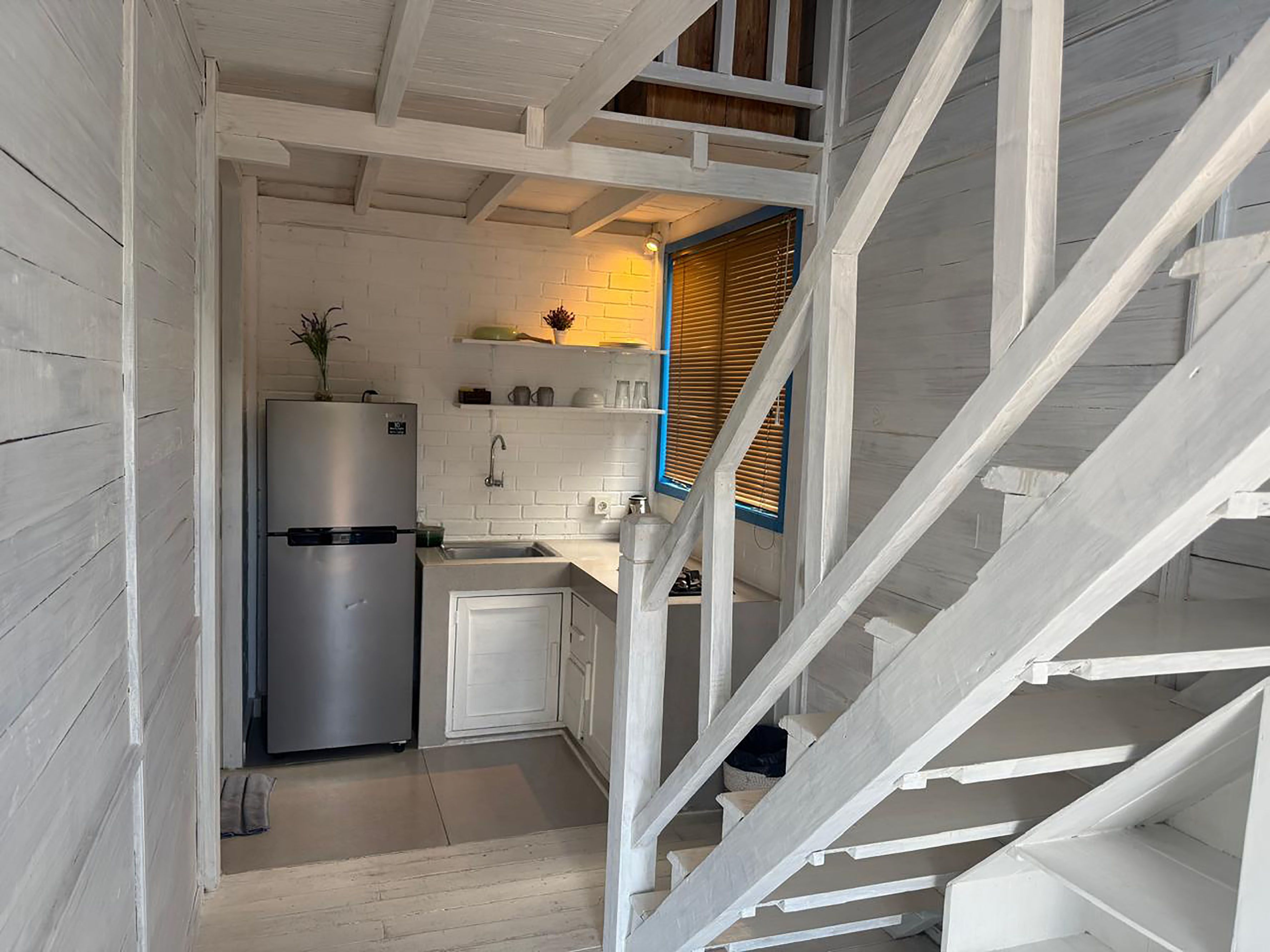 Une cuisine compacte équipée d’un réfrigérateur, d’un évier et de placards, donnant accès à un escalier.