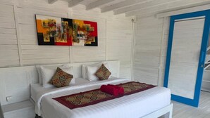 Ein Bett mit weißer Bettwäsche und einer roten Decke, ein gemustertes Teppich und ein farbenfrohes abstraktes Gemälde an der Wand.