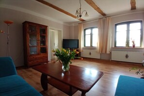 A living room with a wooden table, blue sofas, a cabinet, a television, and a window with curtains. - Holiday apartment with 2 bedrooms (Mirow\/ Ortsteil Babke)