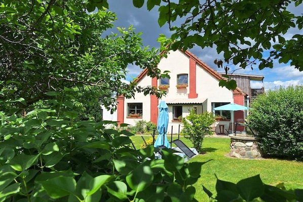 Ein zweistöckiges Haus mit rotem Dach, einem Balkon und einem Garten mit Trampolin und Gartenmöbeln.