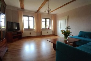 A living room with wooden floors, a television, a sofa, a coffee table, and a plant. - Holiday apartment with 2 bedrooms (Mirow\/ Ortsteil Babke)